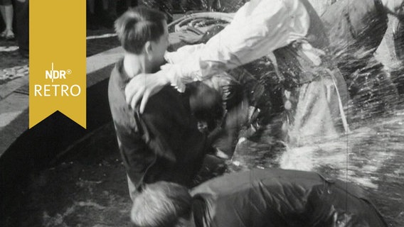 Junge Männer plantschen in einem Brunnen bei der rituellen Wassertaufe der Handwerksgesellen in Husum (1964)  