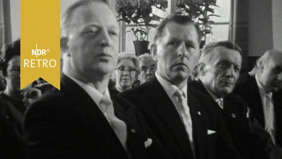 Mehrere Männer in Anzügen in der ersten Reihe beim Festakt zum 100-jährigen Bestehen des Männergesangsvereins Leck (1964)  