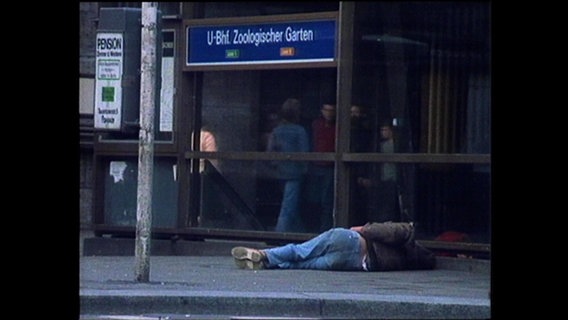 Eine Person liegt vor dem Bahnhof Zoo  