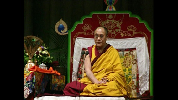 Der Dalai Lama sitzt auf einer Empore  