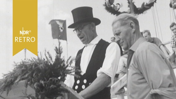 Zimmerleute bei Rede zum Richtfest, im Hintergrund schwebt die Richtkrone (1964)  