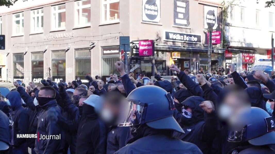 Eine Polizeikette steht vor einer Gruppe von Fußsballhooligans.