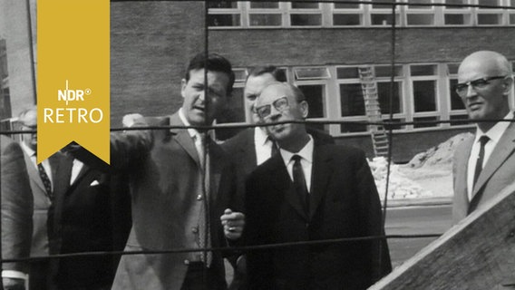 Mehrere Rundfunkräte lassen sich von einem anderen Mann auf einer Baustelle etwas erklären (1964)  