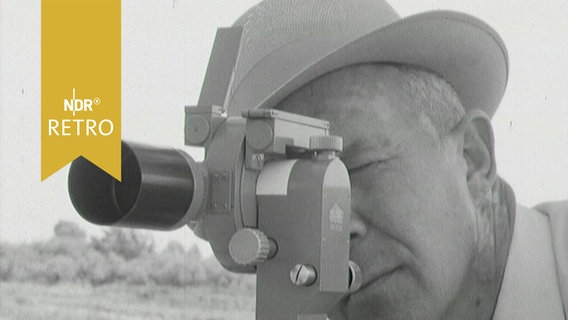 Landvermesser mit einem Theodolit vor dem Gesicht bei der Arbeit (1964)  