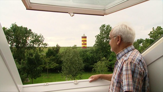 Erhard Jüsche blickt aus einem Fenster auf einen gelbroten Leuchtturm © Screenshot 