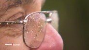 Nahaufnahme einer mit Regentropfen benässte Brille auf einer Nase eines Mannes im Profil © Screenshot 