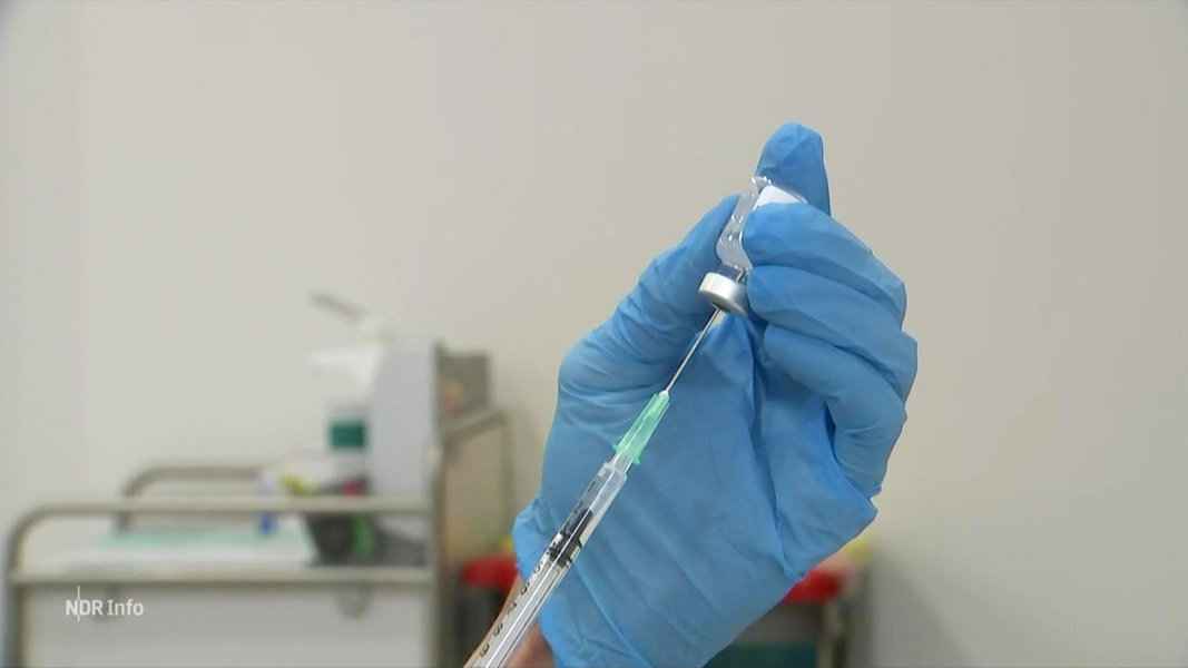 Zwei Hände in Latexhandschuhen ziehen eines Impfspritze aus einer Ampulle auf.