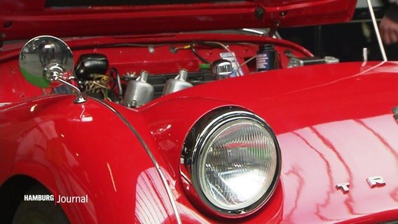 Nahaufnahme eines roten "Triumph" Oldtimers mit geöffneter Motorhaube. © Screenshot 