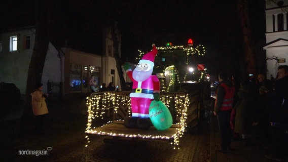 Ein mit Lichterketten dekorierter Bagger trägt eine Weihnachtsmannfigur auf seiner Schippe © Screenshot 