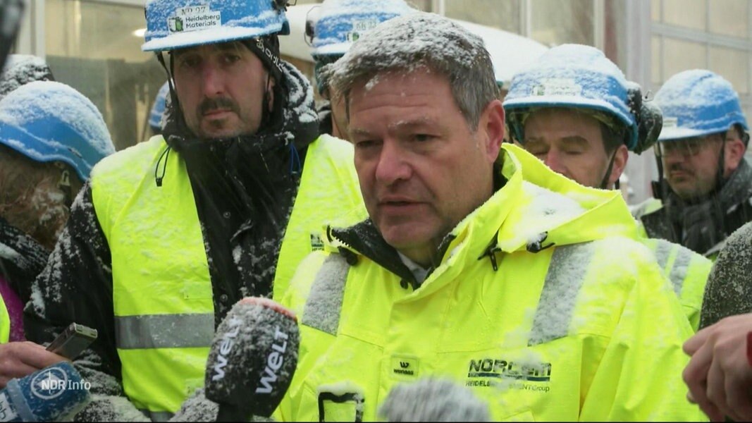 Wirtschaftsminister Habeck im Interview. Erträgt eine gelbe Warnjacke und es schneit, im Hintergrund hören andere zu.