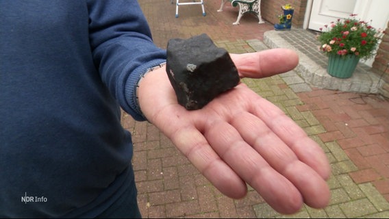 Ein Mann präsentiert einen Meteoriten auf seiner Handfläche, der ihm das Dach durchschlagen hat. © Screenshot 