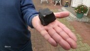 Ein Mann präsentiert einen Meteoriten auf seiner Handfläche, der ihm das Dach durchschlagen hat. © Screenshot 