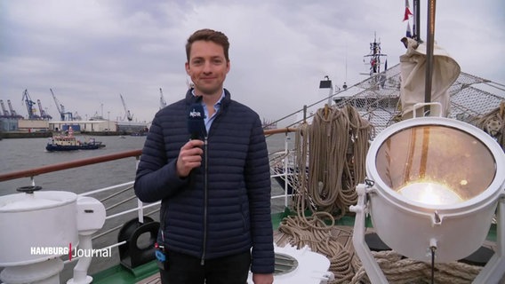 Reporter Simon Ritter steht auf dem Deck eines Schiffes beim Hamburger Hafengeburtstag und blickt in die Kamera. © Screenshot 