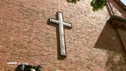 Das Kreuz der katholischen Kirche hängt an einem Kirchengebäude. © Screenshot 