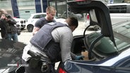 Ermittlungen gegen die Gruppe "Letzte Generation": Polizisten tragen in Hamburg Kartons in ein Auto. © Screenshot 