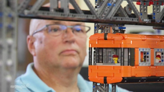 Ein Mann beobachtet eine Schwebebahn aus Lego. © Screenshot 