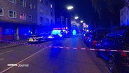 Blick auf eine Straße in einem Stadtteilzentrum bei Nacht: Ein Polizeiabsperrband begrenzt einen Tatort in dem ein Polizeieinsatzfahrzeug mit Blaulicht steht. © Screenshot 