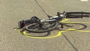 Ein verunfalltes Fahrrad liegt auf der Straße, die Umrisse sind mit gelbem Spray markiert. © Screenshot 