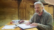 Der Geologe Johannes Jansen mit Papier und Stiften an einem Tisch. © Screenshot 