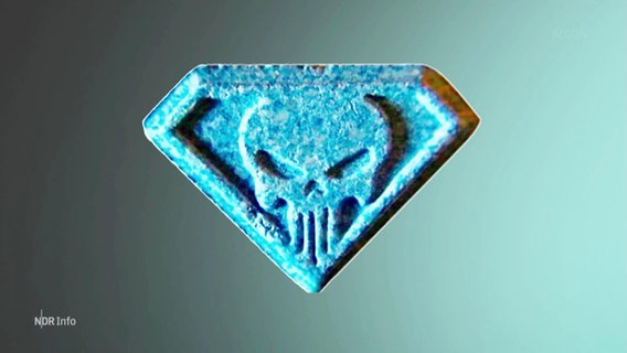 Eine Nahaufnahme einer blau gefärbten Pille mit dem eingeprägten Logo eines Totenkopfschädels. © Screenshot 