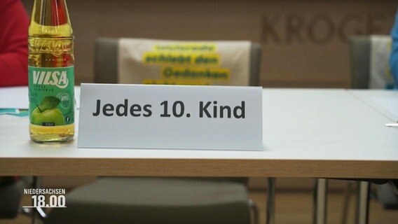 Auf einem Tisch steht ein Aufsteller mit dem Satz: "Jedes 10. Kind". © Screenshot 