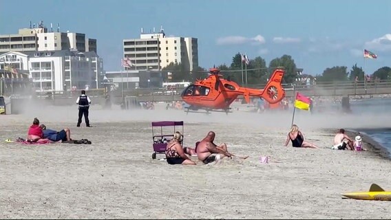 Ein Rettungshubschrauber landet an einem Badestrand. Dabei wirbelt er sehr viel Sand auf. © Screenshot 