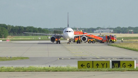 Ein Flugzeug auf dem Hamburger Flughafen, neben dem Fahrzeuge der Feuerwehr stehen. © Screenshot 