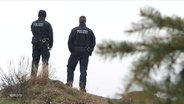 Zwei Polizeibeamte stehen auf einem Hügel. © Screenshot 