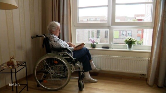 Eine ältere Dame sitzt im Rollstuhl am Fenster ihres Zimmers in einer Pflegeeinrichtung. © Screenshot 