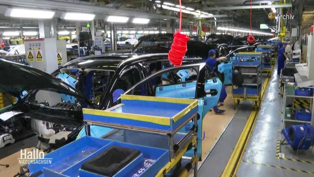 Blick in einer Fabrikstraße einer Auto-Fabrik: Mehrere Mitarbeitende werkeln an noch nicht fertiggestellten Automodellen.