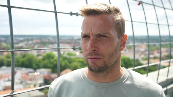 Der Trainer des Greifswalder FC, Lars Fuchs, im Interview auf einer Aussichtsplattform über einer Kleinstadt. © Screenshot 