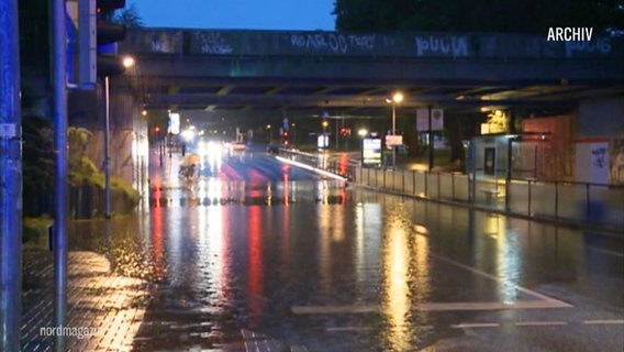 Auf einer Straße unter einer Eisenbahnbrücke hat sich bei Dämmerung eine riesige Pfütze nach einem Starkregen gebildet. © Screenshot 