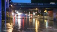Auf einer Straße unter einer Eisenbahnbrücke hat sich bei Dämmerung eine riesige Pfütze nach einem Starkregen gebildet. © Screenshot 