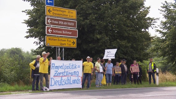 Menschen protestieren mit Schildern gegen eine geplante Unterkunft für geflüchtete Menschen. © Screenshot 