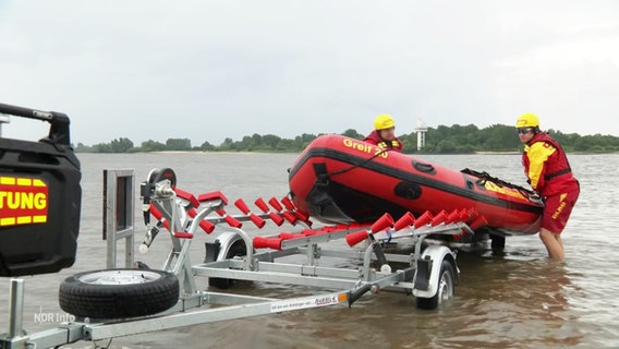 Zwei Mitarbeitende des DLRG hieven am Strand ein Schlauchboot aus dem Wasser auf einen Trailer. © Screenshot 