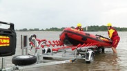 Zwei Mitarbeitende des DLRG hieven am Strand ein Schlauchboot aus dem Wasser auf einen Trailer. © Screenshot 