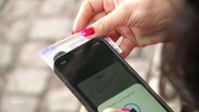 Jemand hält einen Personalausweis auf die Rückseite eines Smartphones. © Screenshot 