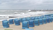 Ein Strand mit stürmischen Wellen und vielen leeren, blauen Strandkörben. © Screenshot 