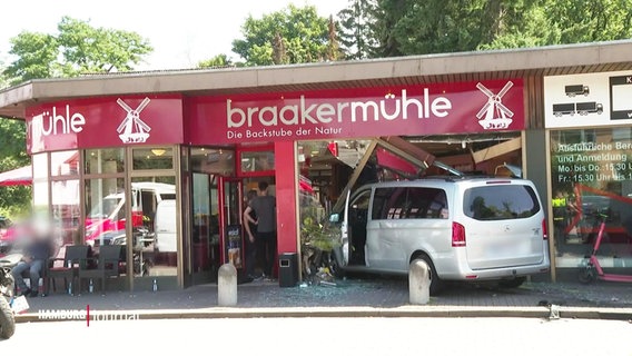 Ein Silberner Transporter steckt nach einem Unfall in der Ladenfront einer Bäckerei. © Screenshot 