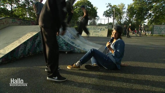 Reporterin Birgit Stamerjohanns sitzt auf dem Boden in einem Skatepark. Auf dem Kopf trägt sie einen Skatehelm und lächelt in die Kamera. © Screenshot 