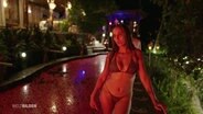 Eine junge Frau in Bikini vor einem Pool im Abendlicht. © Screenshot 