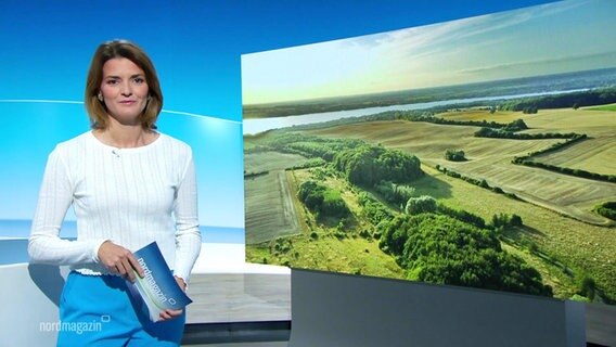 Nachrichtensprecherin Frauke Rauner, im Hintergrund eine Luftaufnahme von einer naturbelassenen Landschaft. © Screenshot 