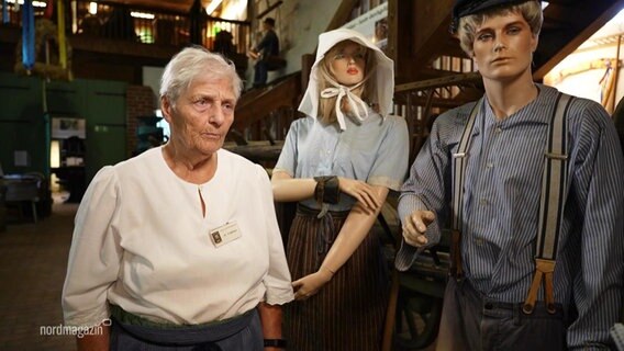 Eine Frau steht neben zwei Schaufensterpuppen, die Kleidung aus einem anderen Jahrhundert tragen. © Screenshot 