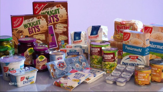 Mehrere Supermarktprodukte in verschiedenen Packungsgrößen stehen nebeneinander auf einem Tisch. © Screenshot 