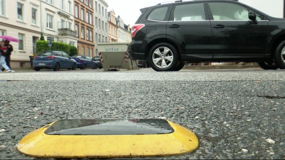 Vor einem parkenden Auto ist auf der Straße ein flaches gelbes Gerät montiert. © Screenshot 