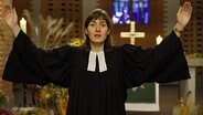 Die Pastorin Fabienne Fronek mit erhobenen Armen bei einer Predigt © Screenshot 