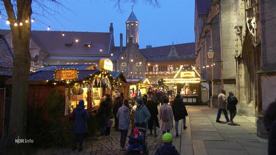 Ein Weihnachtsmarkt vor einer Kirche in der Abenddämmerung. © Screenshot 