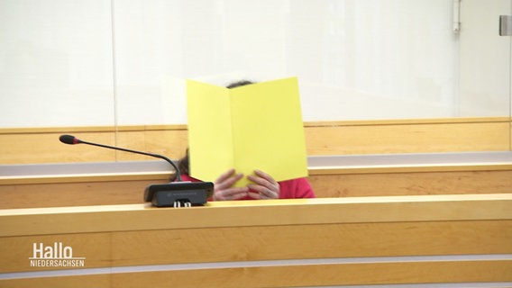 Der Verdächtige verdeckt im Gerichtssaal sein Gedicht mit einer Akte. © Screenshot 