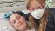 Daniel Gerike in einem Krankenhausbett mit seiner Tochter, die einen Mundschutz trägt. © Screenshot 