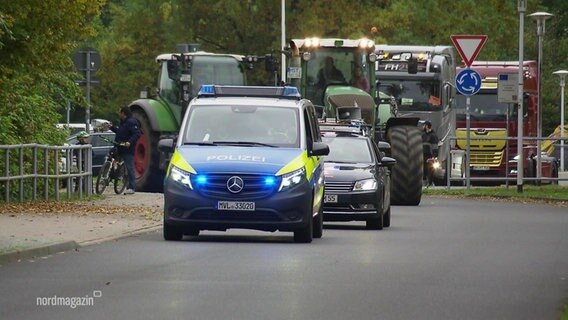 Eine Fahrzeugkolonne, bestehend aus Polizeiautos und Traktoren fährt eine Straße entlang auf die Kamera zu. © Screenshot 